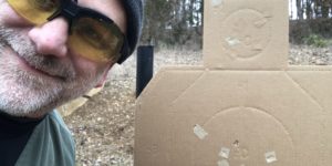 Me pointing to a a single hole made by two shots on a cardboard silhouette target.